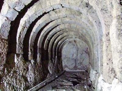 The image shows a stone-vaulted underground passage or tunnel with a metal handrail, likely part of an archaeological site's subterranean structure.