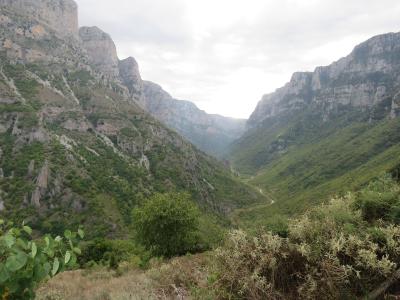 A landscape photograph showing a deep, narrow gorge with steep, rocky cliffs on either side, a river winding through the bottom, and green vegetation covering the slopes, viewed from a high vantage point.