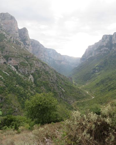 A landscape photograph showing a deep, narrow gorge with steep, rocky cliffs on either side, a river winding through the bottom, and green vegetation covering the slopes, viewed from a high vantage point.