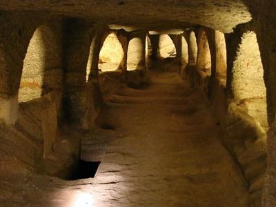 Lamp-lit rock-cut corridor with arched burial niches in the Catacombs of Milos