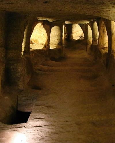 Lamp-lit rock-cut corridor with arched burial niches in the Catacombs of Milos