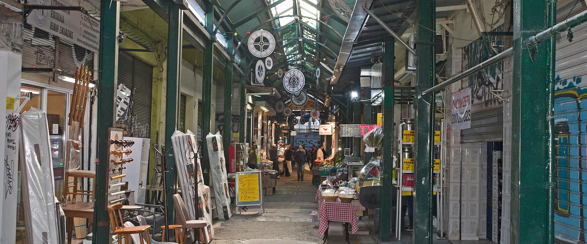A covered market arcade with a green metal arched roof, skylights, and shops lining a paved walkway.