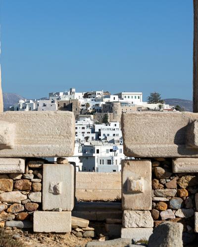 The image shows the massive marble pillars and entablature of the Temple of Apollo at the Portara, with the white-washed buildings of Naxos Chora visible in the background.