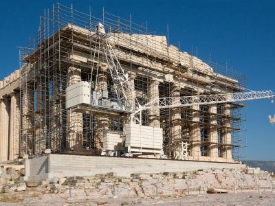 A large ancient Greek temple with Doric columns, heavily covered in scaffolding and construction equipment, indicating active restoration work.