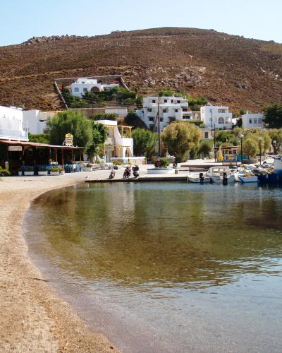A coastal scene showing a small harbor with white buildings, boats, and a pebbly beach under a hillside.