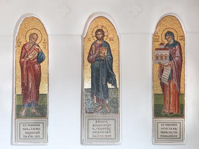 Three vertical religious mosaics depicting saints (including Christ and Saint John the Theologian) mounted on a white interior wall, with Greek inscriptions at the base indicating a 1995 dedication.