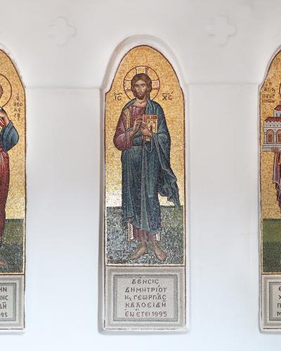 Three vertical religious mosaics depicting saints (including Christ and Saint John the Theologian) mounted on a white interior wall, with Greek inscriptions at the base indicating a 1995 dedication.
